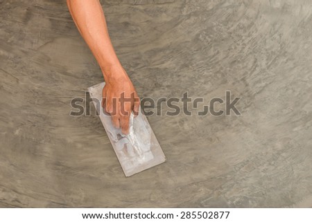 Close up of hand using steel trowel to finish wet concrete floor of polished concrete surface