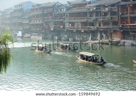 FENGHUANG - OCT 13:Wooden boat with tourists and woddens houses at tuojiang river in fenghuang ancient town on Oct 13, 2013 in Fenghuang,China.