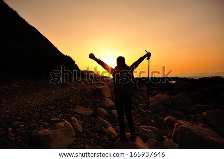 cheering hiking woman raised arms to the sunrise in the morning at seaside