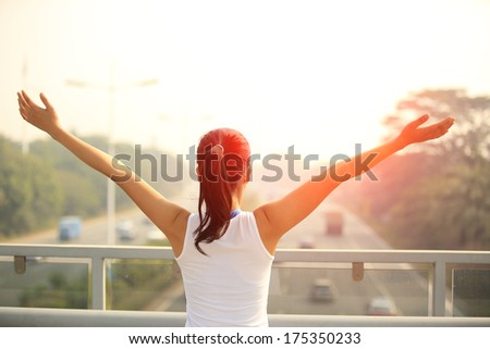 sporty woman stand at the pedestrian overpass open arms to the rush driveway in modern city