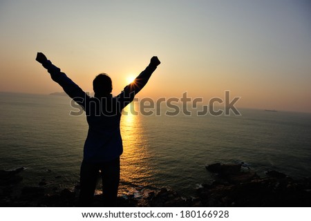 cheering hiking woman open arms to the sunrise stand at seaside mountain