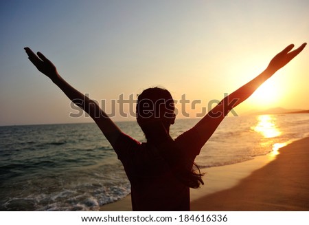 cheering woman open arms to sunrise at seaside