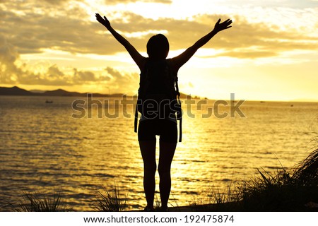 cheering woman hiker open arms to the sunrise stand at seaside