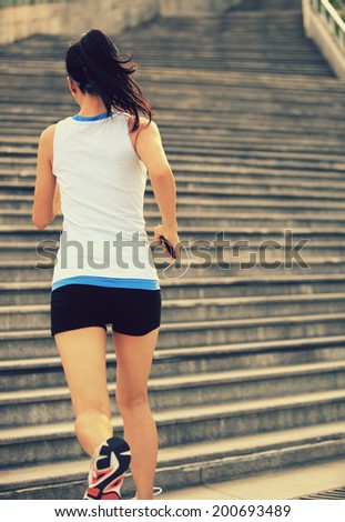 Runner athlete running on stairs. listening to music in headphones from smart phone mp3 player woman fitness jogging workout wellness concept.