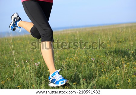 Runner athlete legs running on grass seaside. woman fitness sunrise/sunset jogging workout wellness concept.