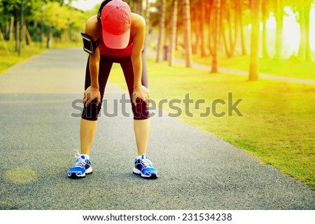 tired woman runner taking a rest after running hard in tropical park trail