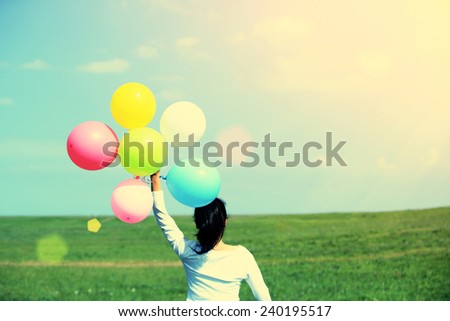 young asian woman running and jumping on green grassland with colored balloons