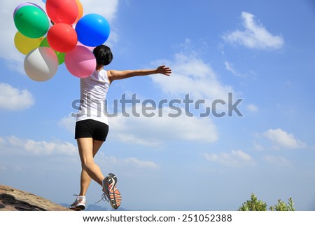 young asian woman running on mountain peak rock with colored balloons