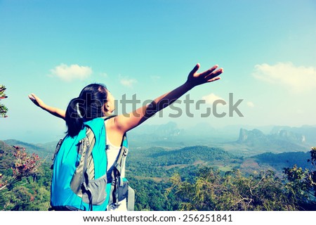 young cheering woman hiker open arms at mountain peak