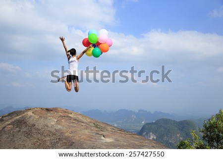 young asian woman jumping on mountain peak rock with colored balloons