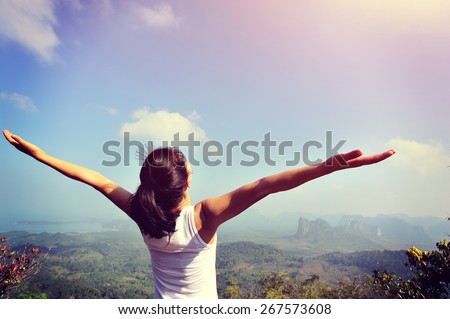 young woman cheering open arms at mountain peak