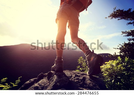 woman hiker legs climbing on sunrise mountain peak rock