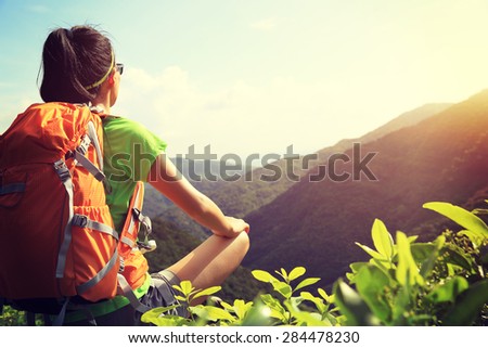 woman backpacker sit on sunrise mountain peak cliff rock enjoy the view