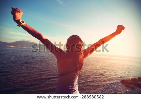 young woman open arms at sunrise seaside