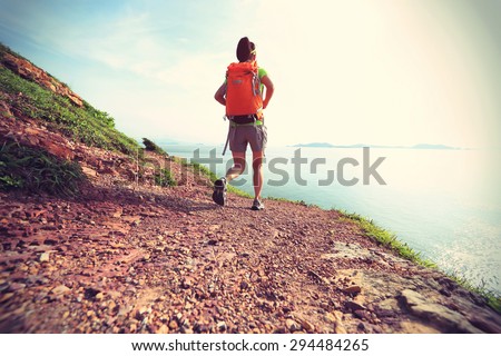 young woman backpacker walking on seaside mountain trail