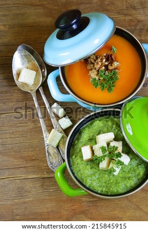 two kinds of cream soup (broccoli and pumpkin) in pot on wooden background