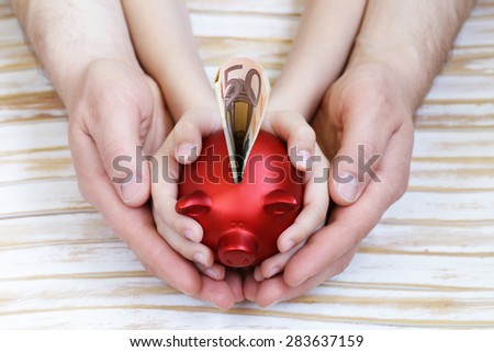close up of father and son hands holding red piggy bank