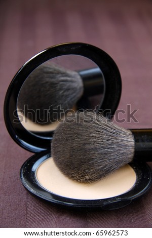 Makeup brush and a box of powder on a brown background