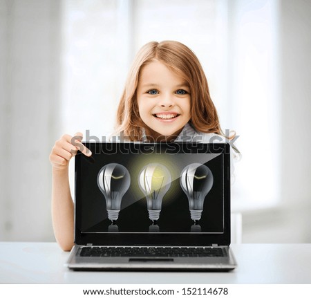 education, school, technology and internet concept - little student girl pointing at laptop pc with light bulbs at school