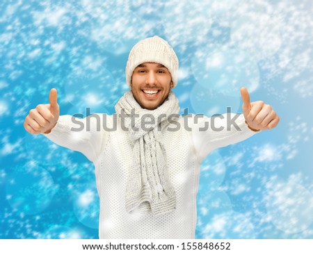 christmas, x-mas, winter, happiness concept - handsome man in warm sweater, hat and scarf showing thumbs up