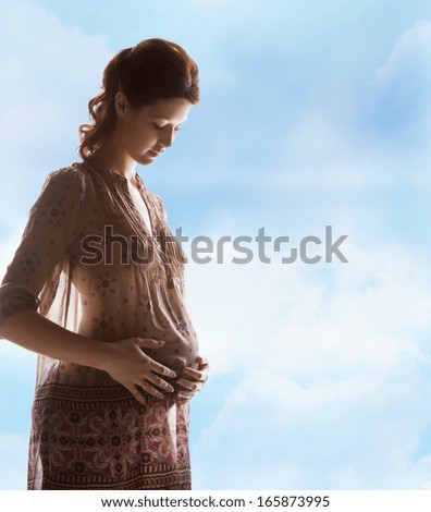 family, motherhood and pregnancy concept - silhouette backlight picture of pregnant beautiful woman touching her belly