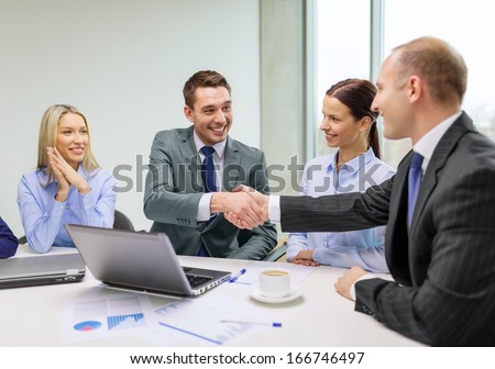 business, technology and office concept - two smiling businessman shaking hands in office