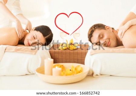spa, beauty, love and happiness concept - smiling couple with candles, flowers and champagne glasses getting massage in spa salon