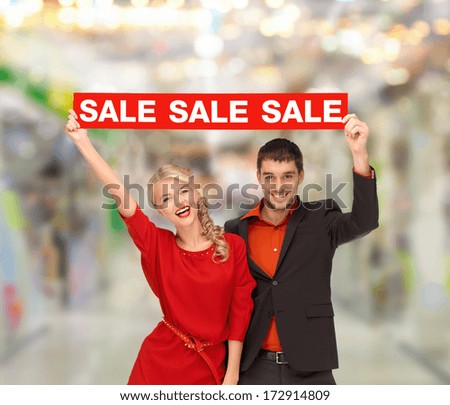 shopping, sale, christmas, couple and mall concept - smiling woman and man with red sale sign at shopping mall