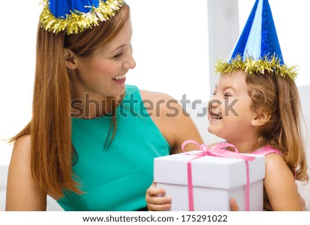 family, children, celebration, holidays, birthday and happy people concept - happy mother and daughter in blue party hats with gift box