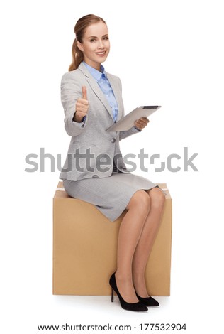 business and delivery service concept - smiling woman sitting on cardboard box with tablet pc computer and showing thumbs up