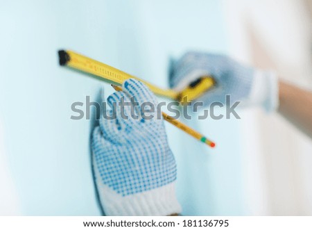 repair, building and home concept - close up of male in gloves measuring wall with tape