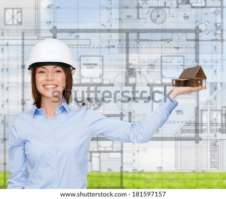 building, developing, advertising and architecture concept - friendly young smiling businesswoman in white helmet holding house on palm