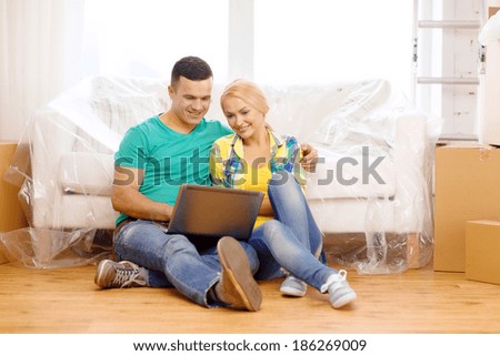 moving, home, technology and couple concept - smiling couple with laptop sitting on floor in new house