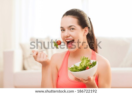healt, dieting, home and happiness concept - smiling sporty teenage girl with green salad at home