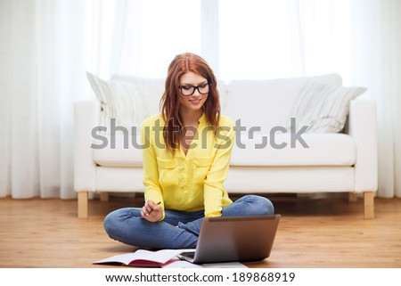 business, education and technology concept - smiling female student in eyeglasses with notebooks and laptop computer at home