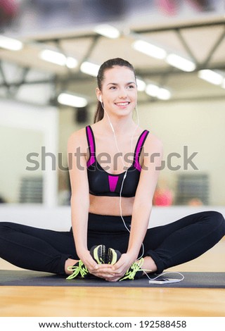 fitness, sport, training, gym and lifestyle concept - smiling teenage girl with earphones stretching on mat in the gym