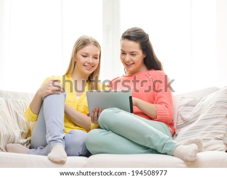 friendship, technology and internet concept - two smiling teenage girls with tablet pc computer at home