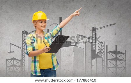 repair, construction and maintenance concept - smiling woman in helmet with construction site on the back with clipboard pointing finger