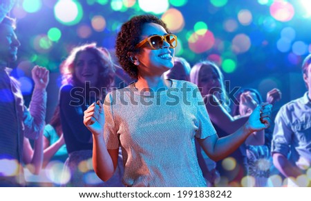 leisure, clubbing and nightlife concept - smiling young african american woman in sunglasses dancing in ultraviolet neon lights over nightclub background