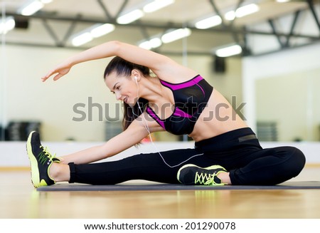 fitness, sport, training, gym and lifestyle concept - stretching young woman with earphones in the gym