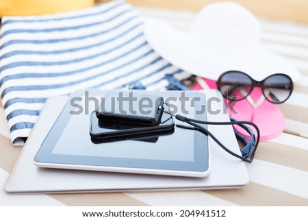 beach, summer, vacation and technology concept - close up of tablet pc computer, smartphone, camera and summer accessories on beach