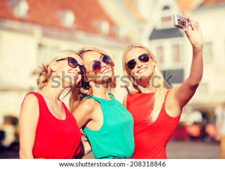 holidays, tourism and modern technology concept - three beautiful girls taking picture with digital camera in the city