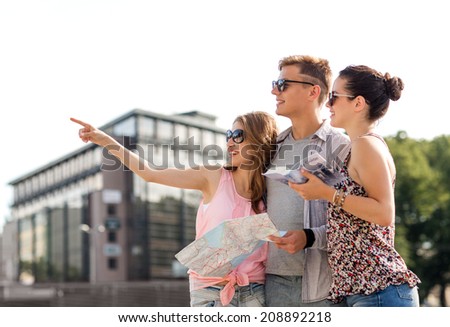 friendship, travel, tourism, vacation and people concept - smiling friends with map and city guide pointing finger outdoors
