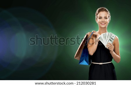 shopping, sale, gifts, money and holidays concept - smiling woman in dress with shopping bags and money over black background