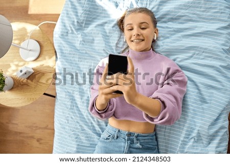 leisure, children and technology concept - happy smiling girl in earphones with smartphone lying on bed at home Foto stock © 