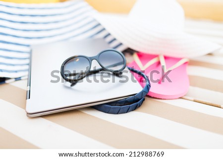 beach, summer, vacation, accessories and technology concept - close up of laptop and summer accessories on beach