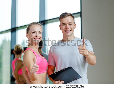 fitness, sport, exercising and diet concept - smiling young woman with personal trainer in gym showing thumbs up