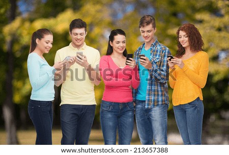 friendship, technology, nature and people concept - group of smiling teenagers with smartphones over park background