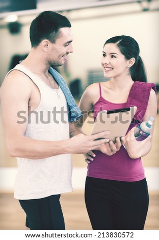 fitness, sport, training, technology and lifestyle concept - two smiling people with tablet pc computer and water bottle in the gym