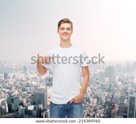 gesture, advertising and people concept - smiling young man in blank white t-shirt pointing finger on himself over city background